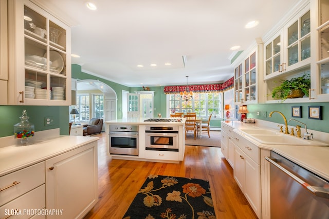 kitchen featuring appliances with stainless steel finishes, light wood-type flooring, sink, pendant lighting, and white cabinets