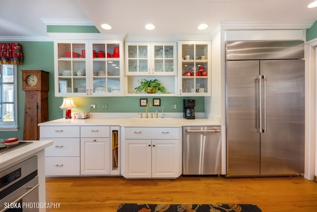 kitchen with white cabinets, sink, crown molding, light hardwood / wood-style flooring, and stainless steel appliances