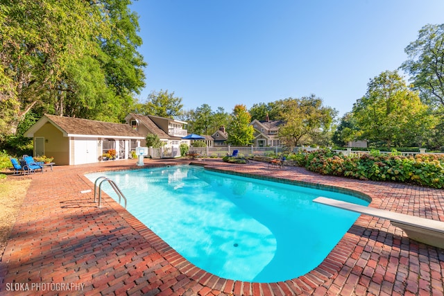 view of pool featuring a diving board, an outbuilding, and a patio