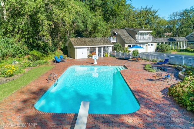 view of swimming pool with a diving board, an outbuilding, and a patio