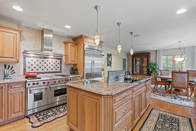 kitchen with wall chimney exhaust hood, a center island with sink, light wood-type flooring, high quality appliances, and pendant lighting