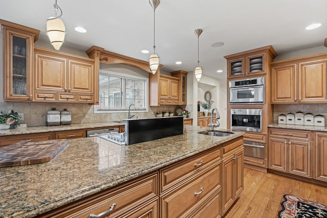 kitchen featuring hanging light fixtures, sink, light stone counters, and light hardwood / wood-style floors