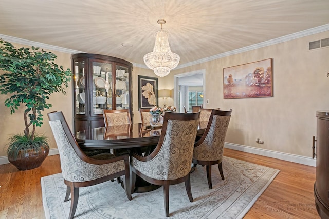 dining space with ornamental molding, a chandelier, and light hardwood / wood-style flooring