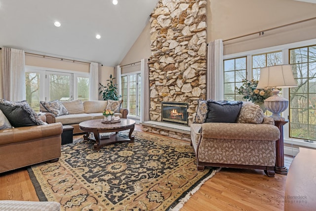 living room with hardwood / wood-style floors, a stone fireplace, and high vaulted ceiling