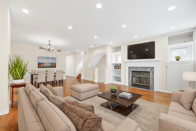 living room featuring built in shelves, an inviting chandelier, light wood-type flooring, and a high end fireplace