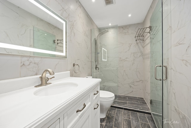 bathroom with tile walls, a shower with shower door, vanity, and toilet