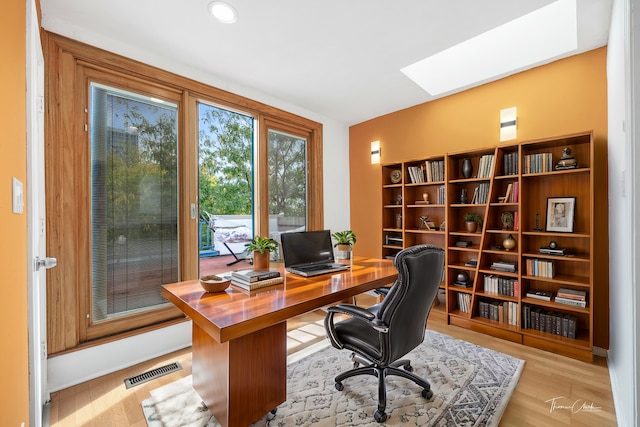 home office with light wood-type flooring and a skylight