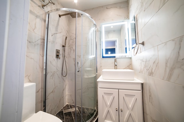 bathroom with tile walls, a shower with door, vanity, and toilet