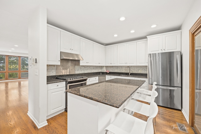 kitchen featuring appliances with stainless steel finishes, light hardwood / wood-style floors, a center island, and exhaust hood