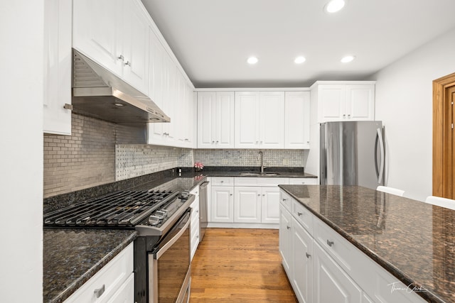 kitchen featuring light hardwood / wood-style floors, sink, white cabinetry, appliances with stainless steel finishes, and dark stone countertops