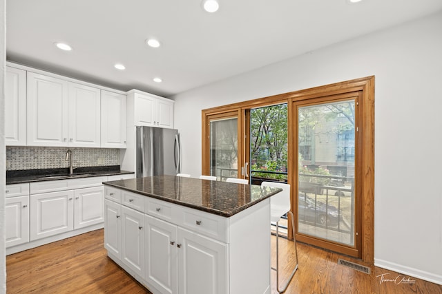 kitchen with light hardwood / wood-style floors, tasteful backsplash, white cabinets, stainless steel refrigerator, and sink