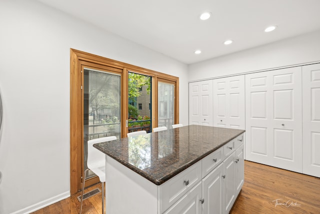 kitchen featuring white cabinets, light wood-type flooring, dark stone counters, and a center island