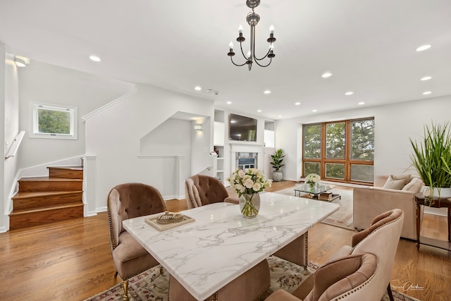 dining space with light hardwood / wood-style flooring, a wealth of natural light, a premium fireplace, and an inviting chandelier