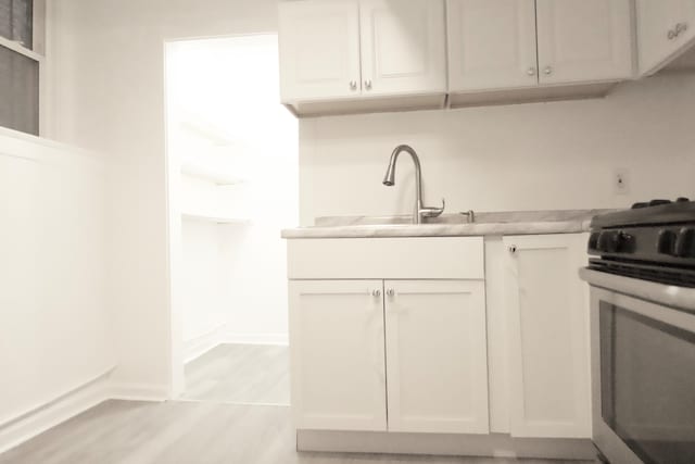 kitchen featuring light wood-type flooring, white cabinets, sink, and stainless steel range