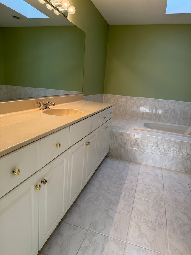 bathroom featuring tiled bath, vanity, and a skylight