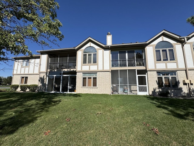 back of house with a chimney, a lawn, brick siding, and stucco siding