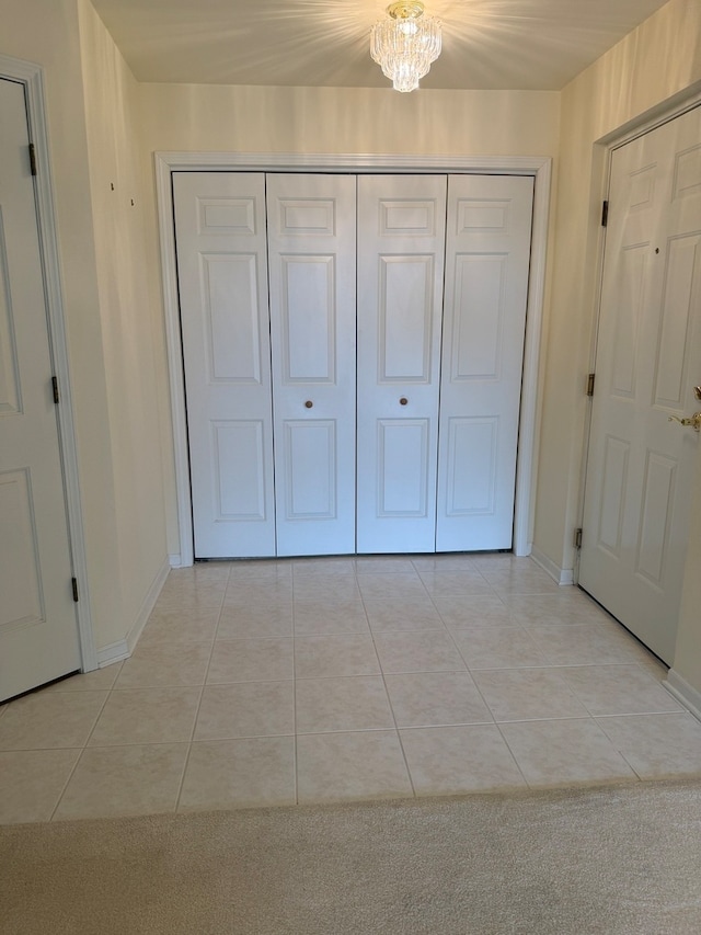 unfurnished bedroom with light tile patterned flooring, baseboards, a closet, and a chandelier