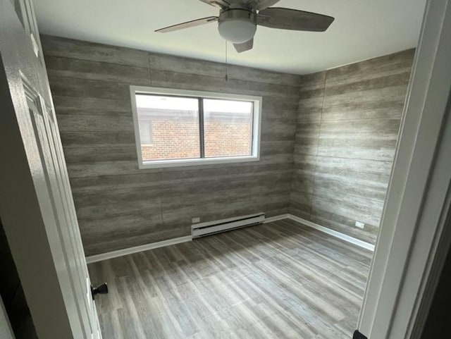 unfurnished room featuring a baseboard radiator, wooden walls, wood-type flooring, and ceiling fan