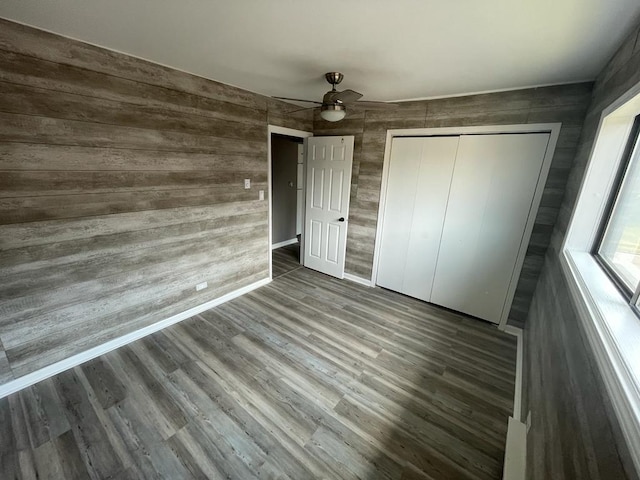 unfurnished bedroom with a closet, wood walls, wood-type flooring, and ceiling fan