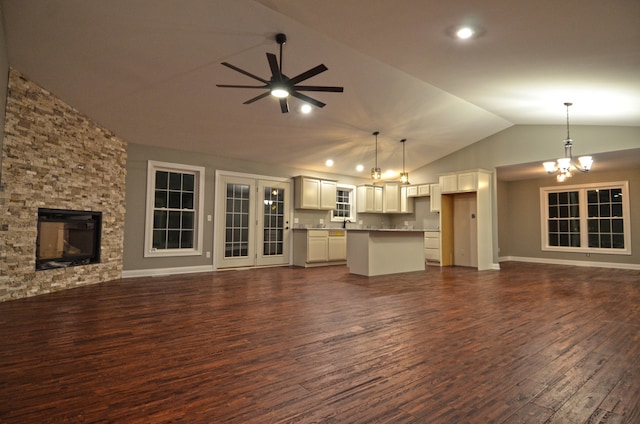 unfurnished living room with dark wood-type flooring, sink, ceiling fan with notable chandelier, vaulted ceiling, and a stone fireplace