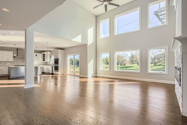 unfurnished living room featuring a towering ceiling, ceiling fan, a fireplace, and dark hardwood / wood-style flooring