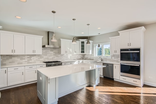 kitchen with wall chimney exhaust hood, white cabinets, appliances with stainless steel finishes, and dark hardwood / wood-style flooring