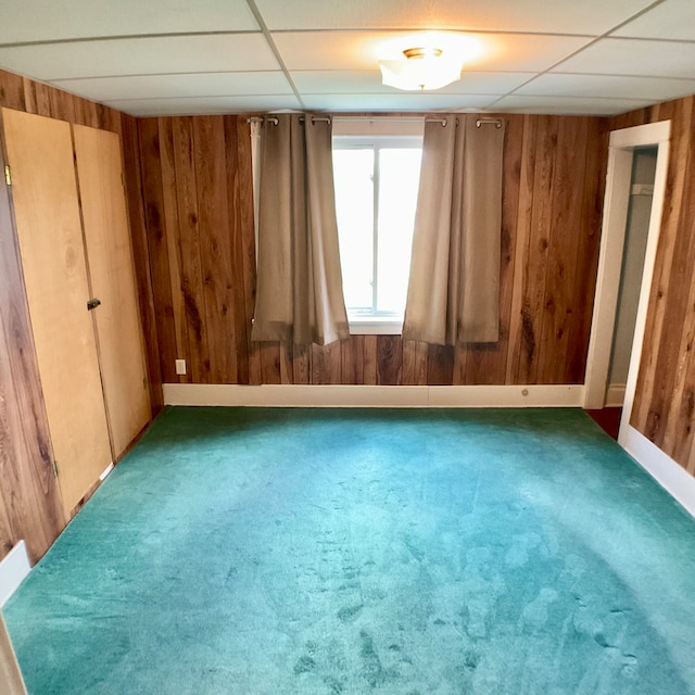 unfurnished room with a drop ceiling, wooden walls, and carpet