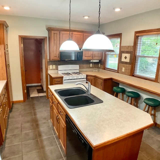 kitchen featuring sink, decorative light fixtures, a kitchen island with sink, black appliances, and decorative backsplash