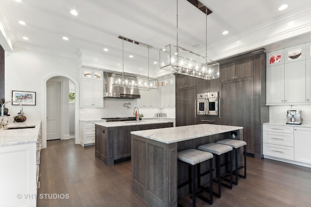 kitchen with wall chimney range hood, a kitchen island with sink, tasteful backsplash, dark wood-type flooring, and sink