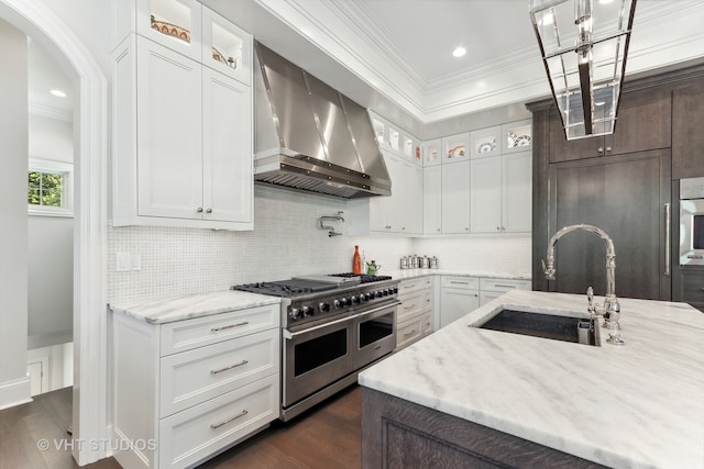 kitchen featuring double oven range, wall chimney range hood, sink, and white cabinetry