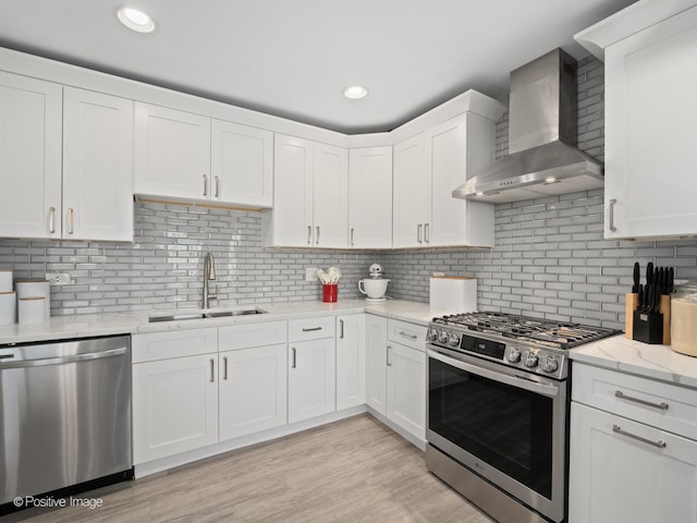 kitchen with sink, white cabinets, wall chimney range hood, light hardwood / wood-style flooring, and stainless steel appliances