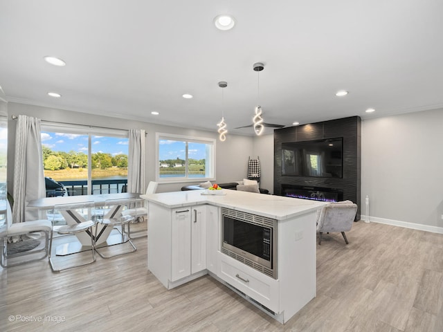 kitchen with white cabinets, decorative light fixtures, crown molding, light wood-type flooring, and stainless steel microwave