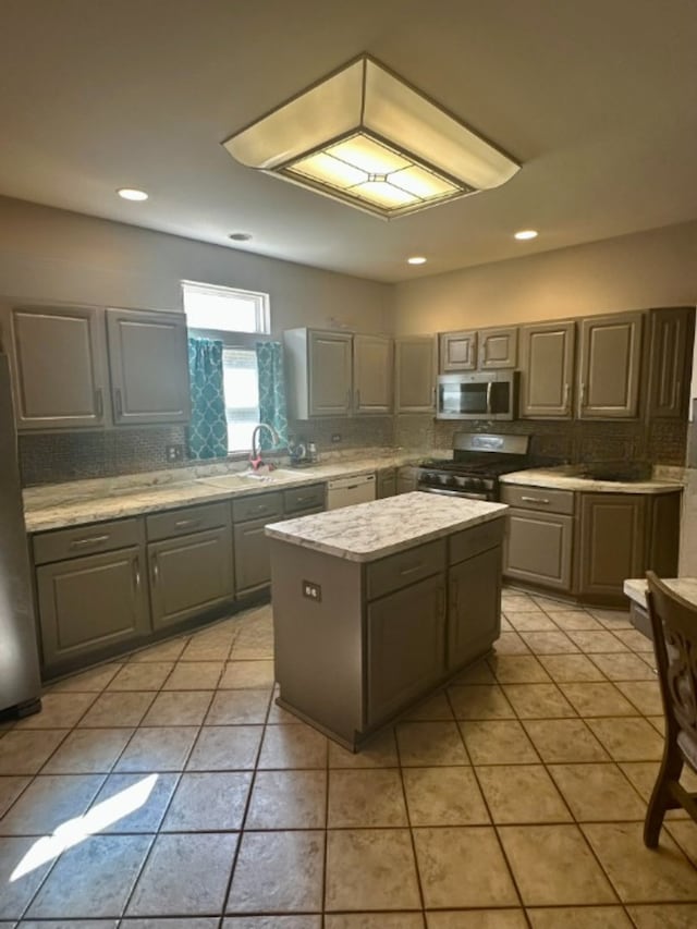 kitchen featuring light tile patterned floors, tasteful backsplash, gray cabinets, a kitchen island, and appliances with stainless steel finishes