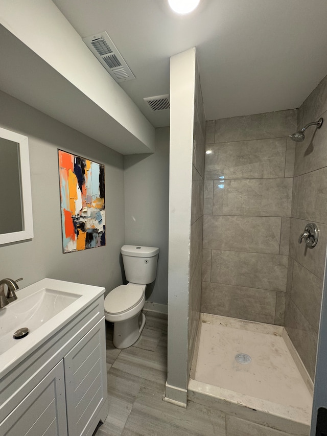 bathroom featuring a tile shower, vanity, toilet, and hardwood / wood-style flooring