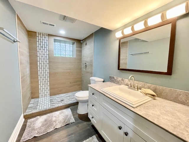 bathroom with a tile shower, hardwood / wood-style flooring, vanity, and toilet