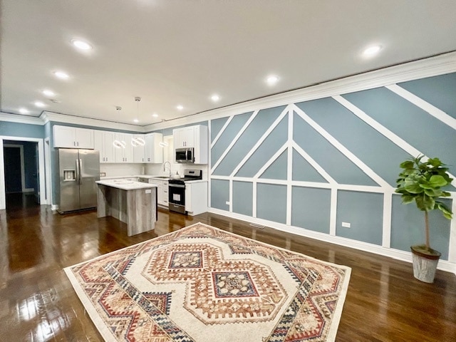 kitchen with pendant lighting, white cabinets, ornamental molding, appliances with stainless steel finishes, and a center island