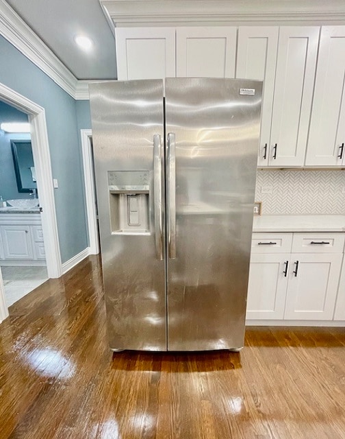 kitchen with tasteful backsplash, white cabinets, crown molding, light hardwood / wood-style flooring, and stainless steel fridge with ice dispenser