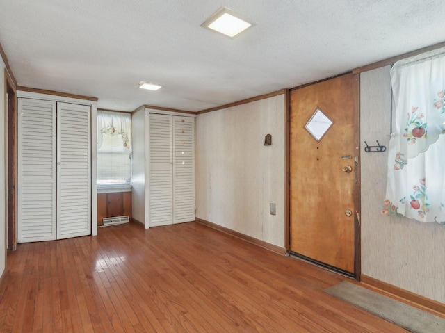 interior space featuring wood-type flooring, a textured ceiling, two closets, and crown molding