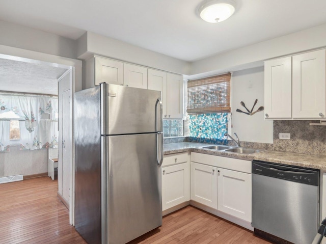 kitchen with sink, tasteful backsplash, light hardwood / wood-style floors, white cabinets, and appliances with stainless steel finishes