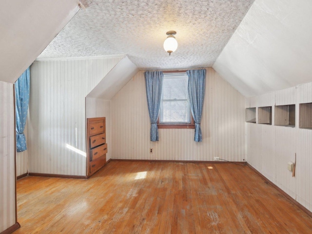 bonus room featuring a textured ceiling, vaulted ceiling, and light hardwood / wood-style flooring