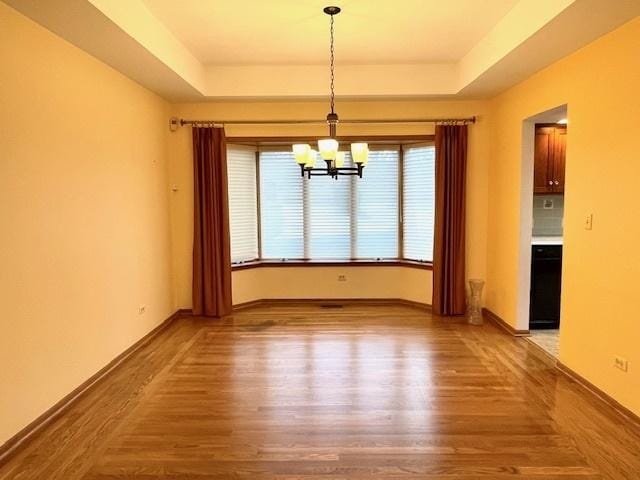 unfurnished dining area featuring a tray ceiling, a chandelier, and hardwood / wood-style flooring