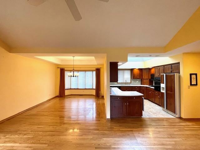 kitchen featuring light hardwood / wood-style flooring, refrigerator with ice dispenser, pendant lighting, a tray ceiling, and ceiling fan with notable chandelier