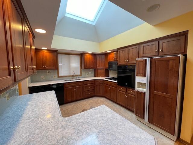 kitchen with kitchen peninsula, backsplash, vaulted ceiling with skylight, black appliances, and sink