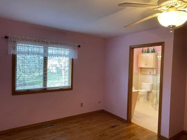 unfurnished bedroom featuring wood-type flooring, ensuite bathroom, and ceiling fan