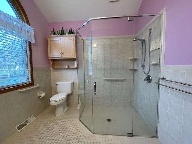 bathroom with an enclosed shower, tile patterned floors, toilet, and tile walls