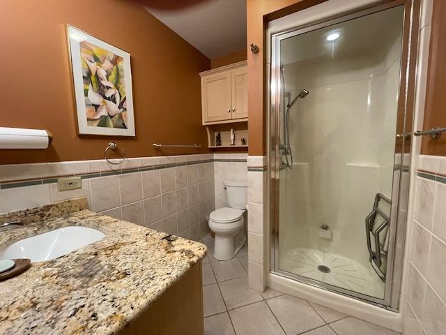 bathroom featuring toilet, tile patterned floors, tile walls, and a shower with shower door