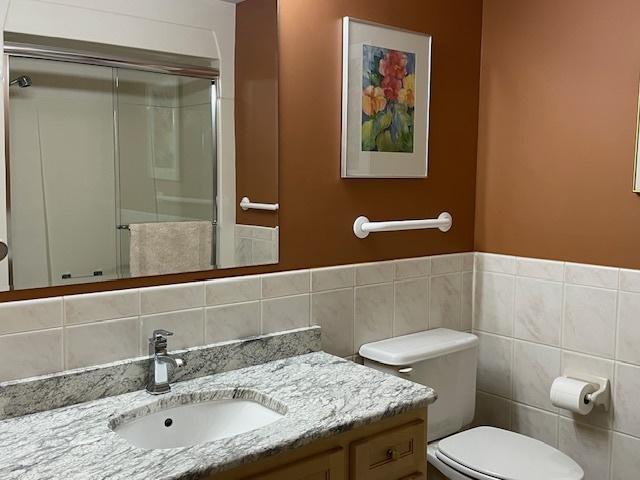 bathroom featuring vanity, toilet, a shower with door, and tile walls