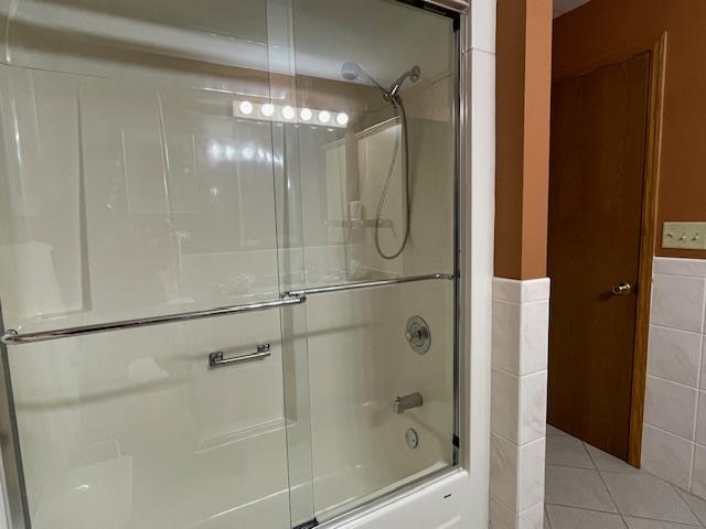 bathroom featuring tile patterned flooring, bath / shower combo with glass door, and tile walls