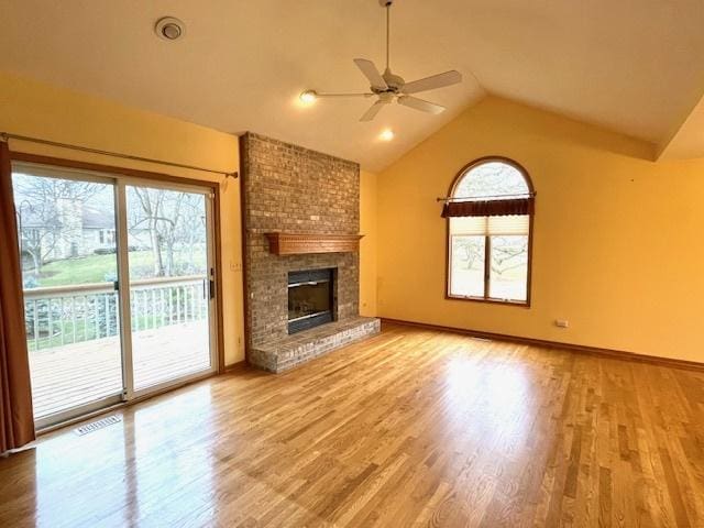 unfurnished living room featuring light hardwood / wood-style floors, lofted ceiling, a fireplace, and a wealth of natural light