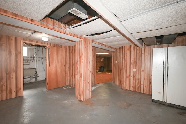 basement featuring white refrigerator and wood walls